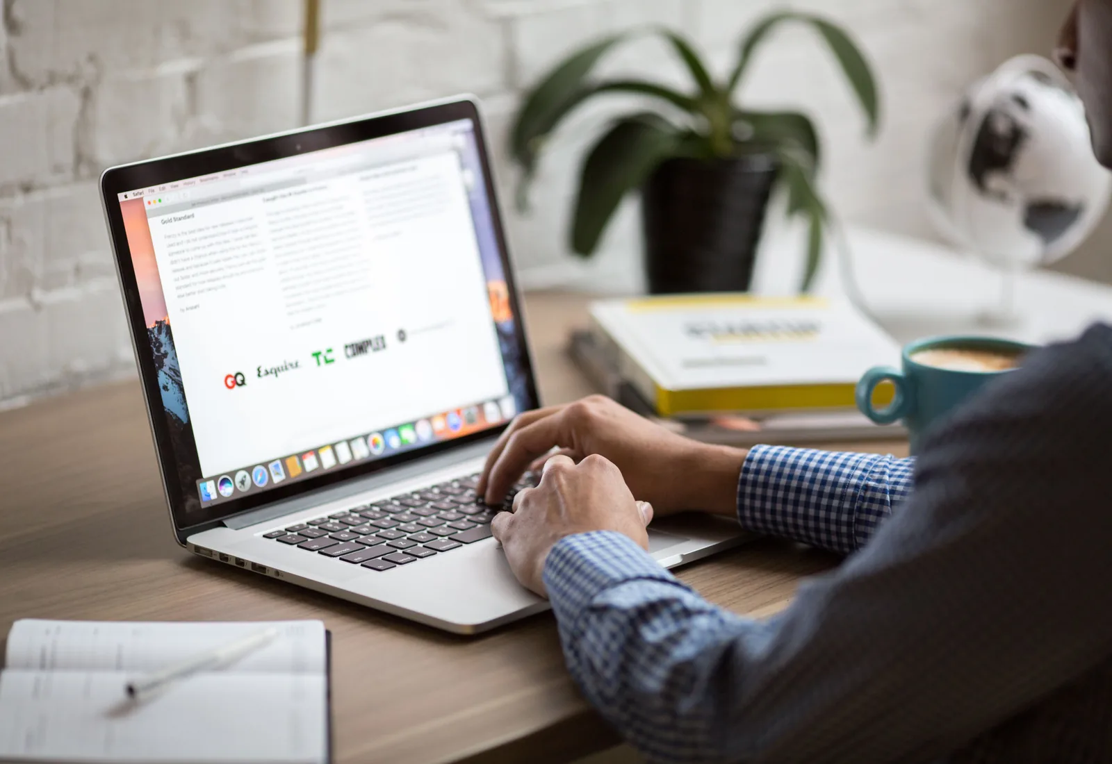 A laptop open on a desk showing an email inbox, beside a notebook and coffee