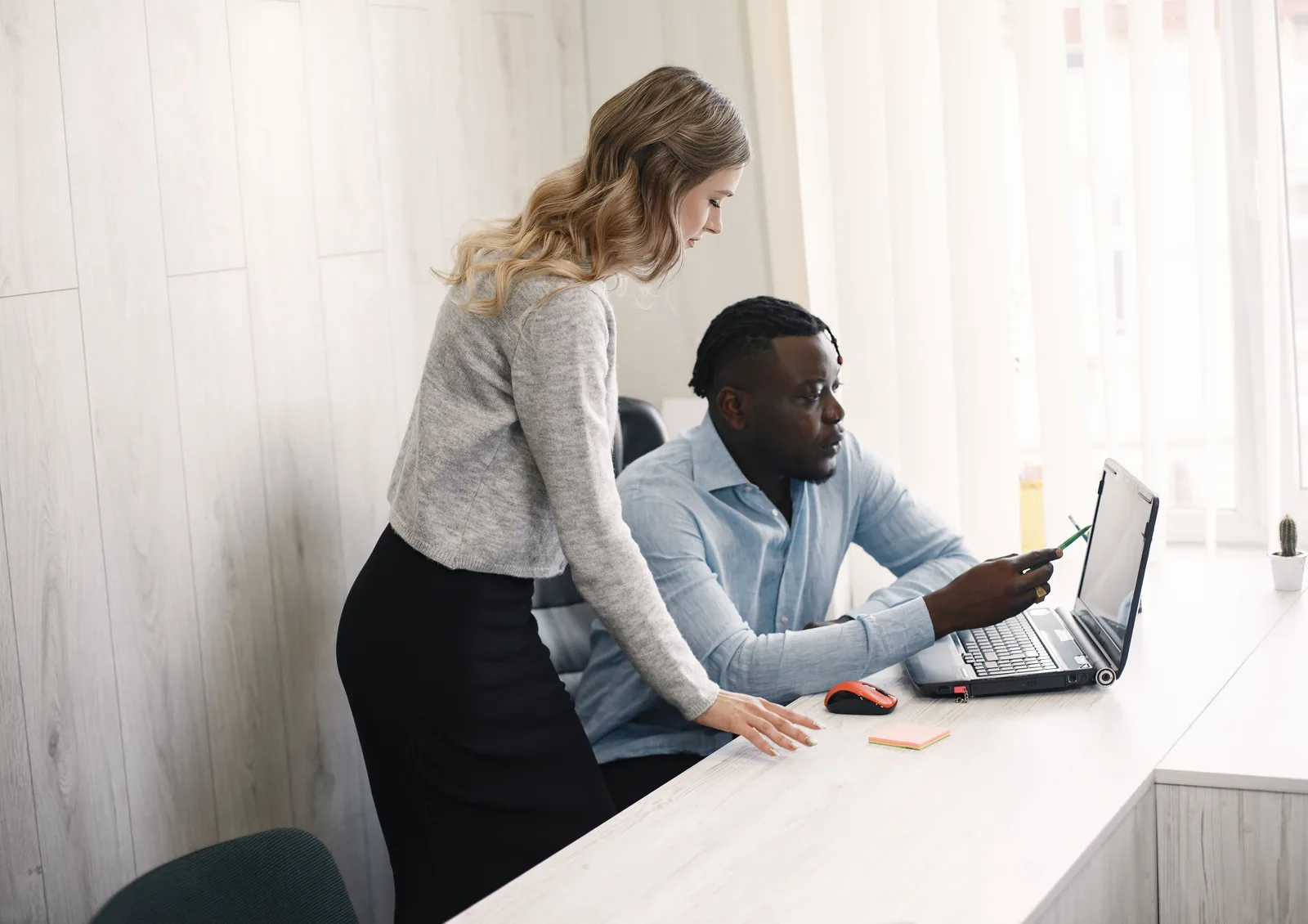 An IT technician helping a colleague at his laptop in a bright office